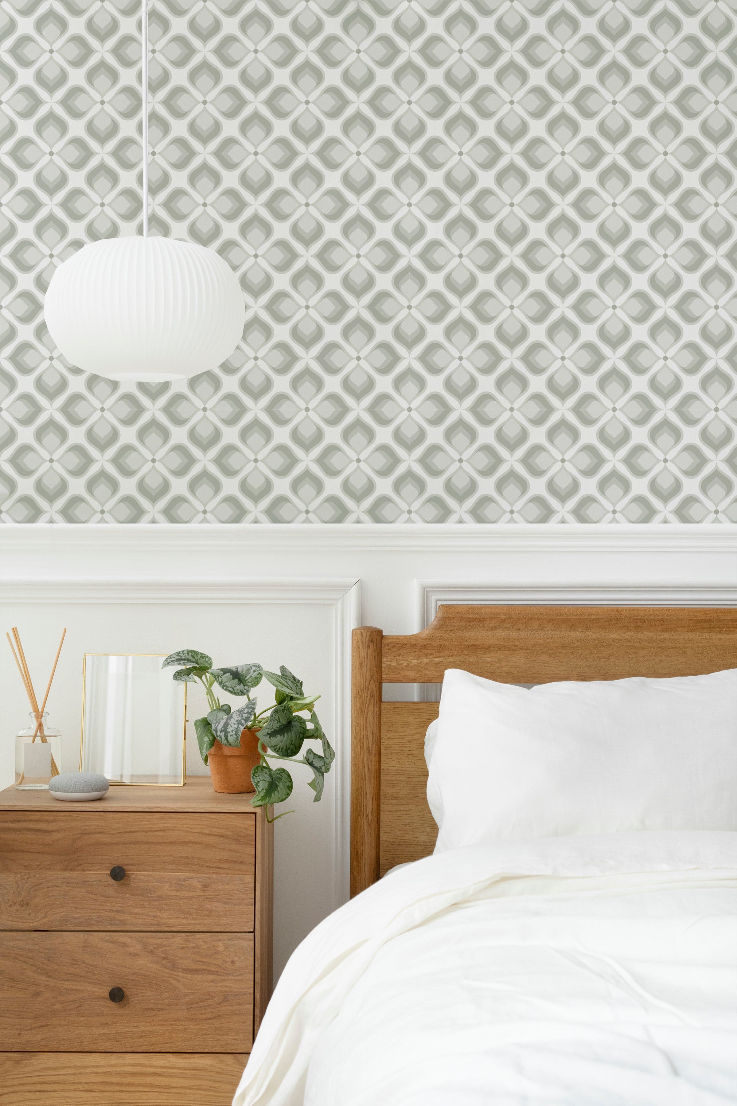 A bedroom setting featuring the Geometric Groove Wallpaper with a subtle, olive-toned geometric pattern. The wallpaper adds a sophisticated touch above the white wainscoting, complemented by a modern wooden bed, a white pendant light, and a dresser adorned with plants and decor items