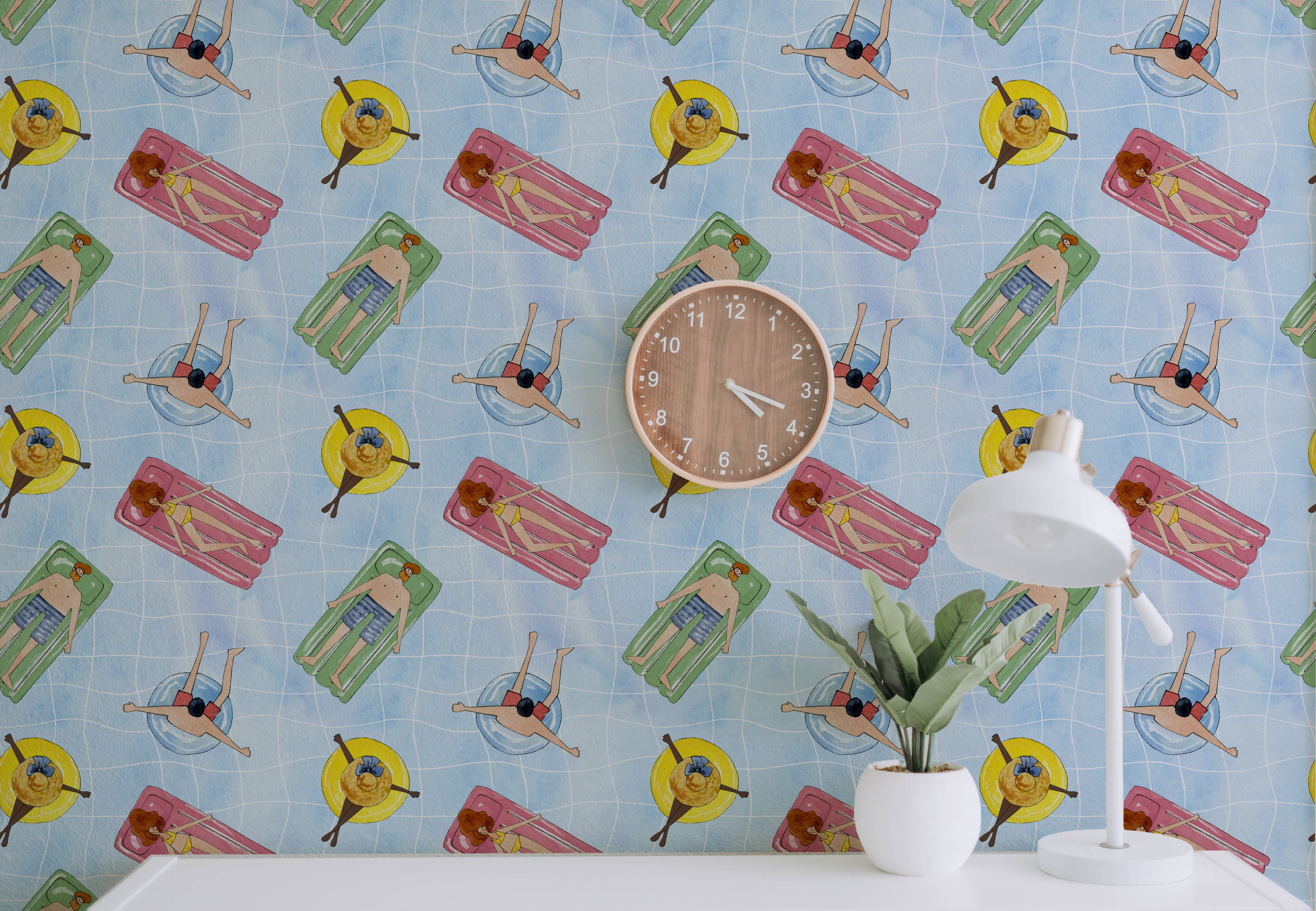 A lively room featuring the Pool Party Wallpaper with illustrations of people on pool floats. A white desk, lamp, and potted plant add modern accents.