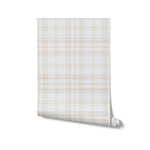 A roll of pastel tartan wallpaper unrolled to display the full pattern. The design features a grid of soft beige, light green, and off-white lines intersecting to create a classic checkered look. The wallpaper roll highlights the smooth texture and the subtle color palette, ideal for adding a refined touch to any room.