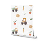 A roll of Farm Friend Wallpaper - Happy Veggies, displaying a charming pattern of yellow tractors, pumpkins, carrots, radishes, and grass on a white background, perfect for adding a touch of fun to any room.