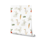 A roll of Farm Friend Wallpaper - Happy Bunnies, displaying a delightful pattern of bunnies, geese, carrots, radishes, and grass on a white background, perfect for adding a playful touch to any room.