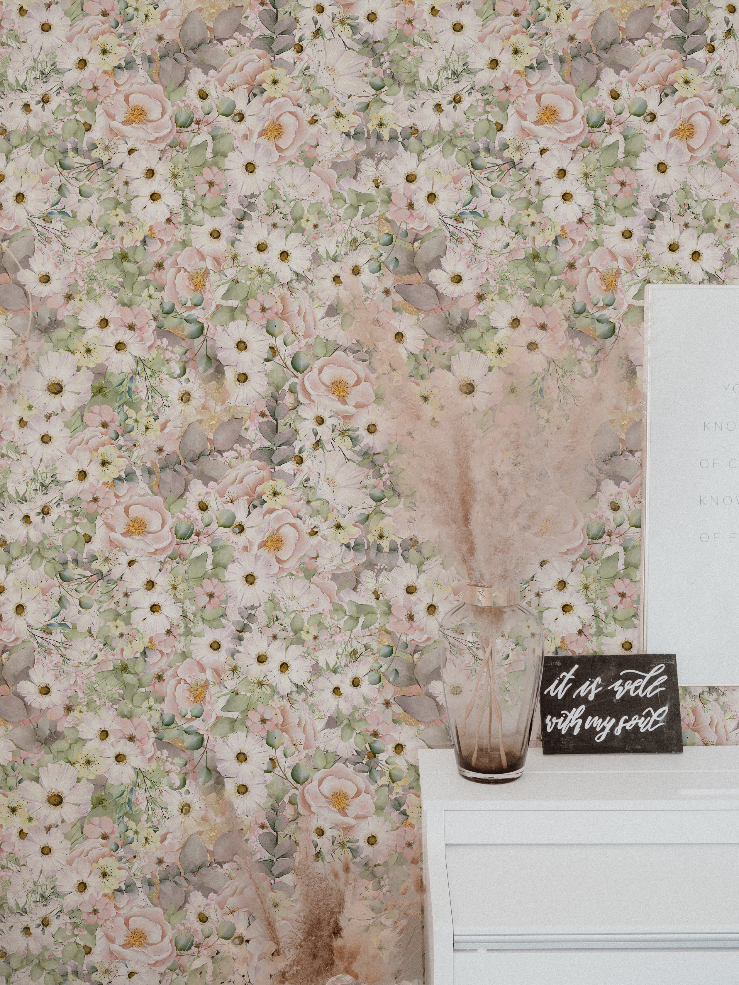 A stylish interior wall decorated with Pink Fleur Wallpaper, which showcases delicate pink and white flowers with touches of green leaves. The wallpaper lends a fresh, botanical vibe to the space, complemented by modern decor elements