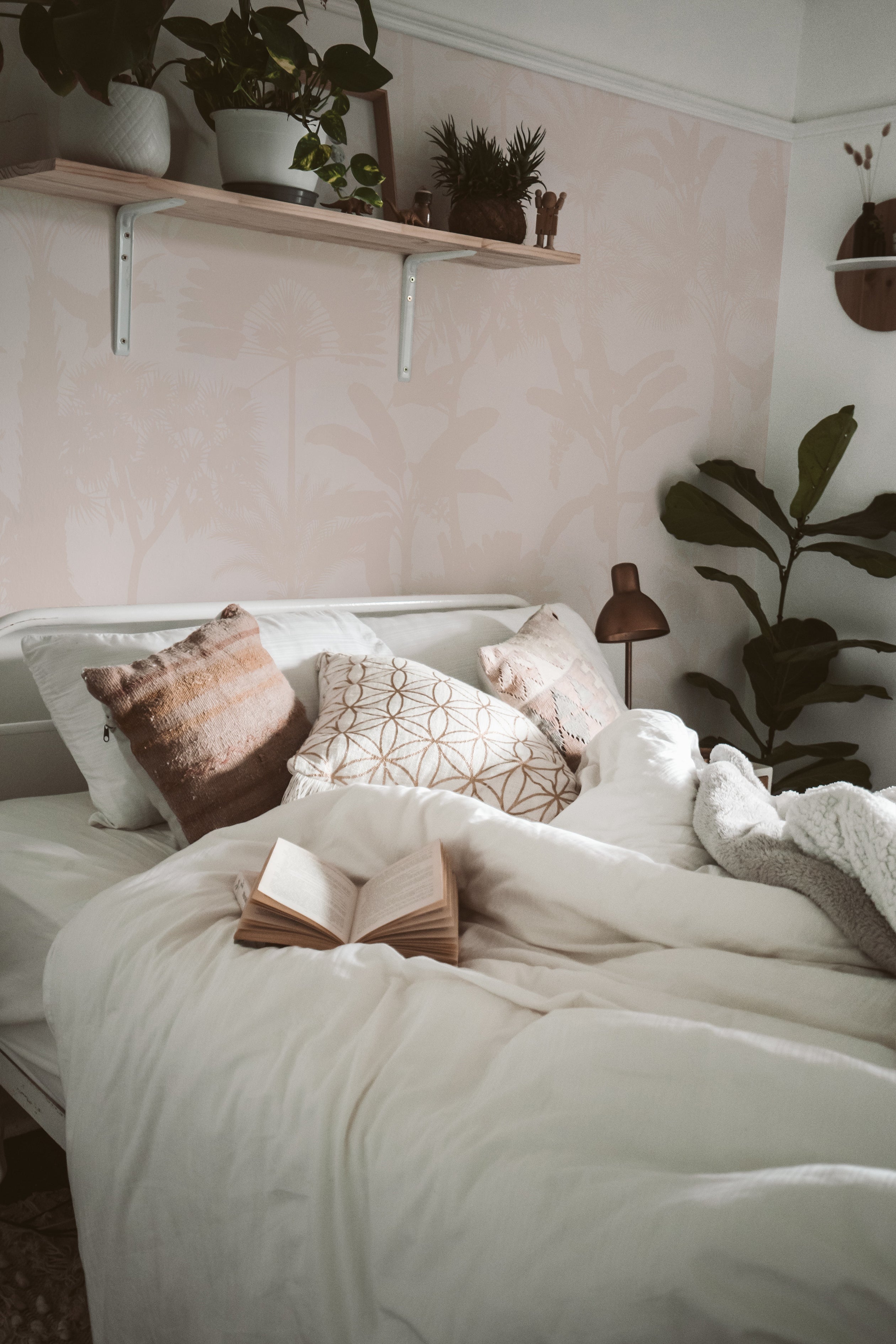 A bedroom enhanced with Exotic Silhouette Wallpaper, displaying a soothing arrangement of white tropical plant silhouettes against a light pink background. The wallpaper adds a gentle, relaxing touch to the space, complemented by earth-toned bedding and natural wood accents