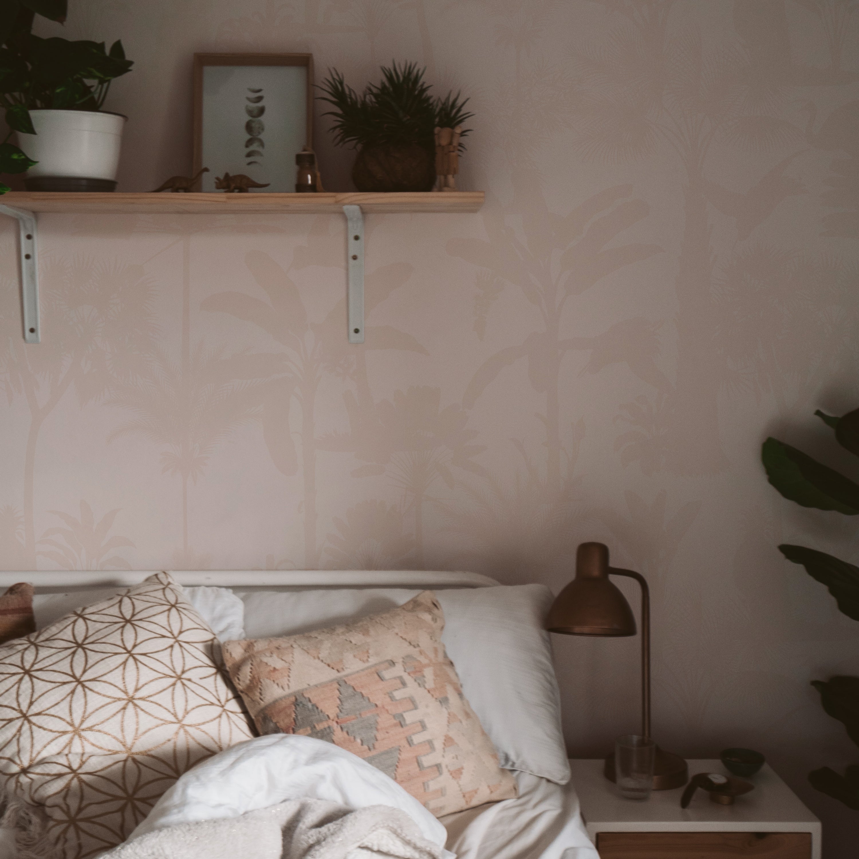 Close-up view of a bedroom wall covered with Exotic Silhouette Wallpaper, highlighting the detailed white silhouettes of tropical foliage on a pastel pink backdrop. This elegant design brings a touch of nature's tranquility indoors