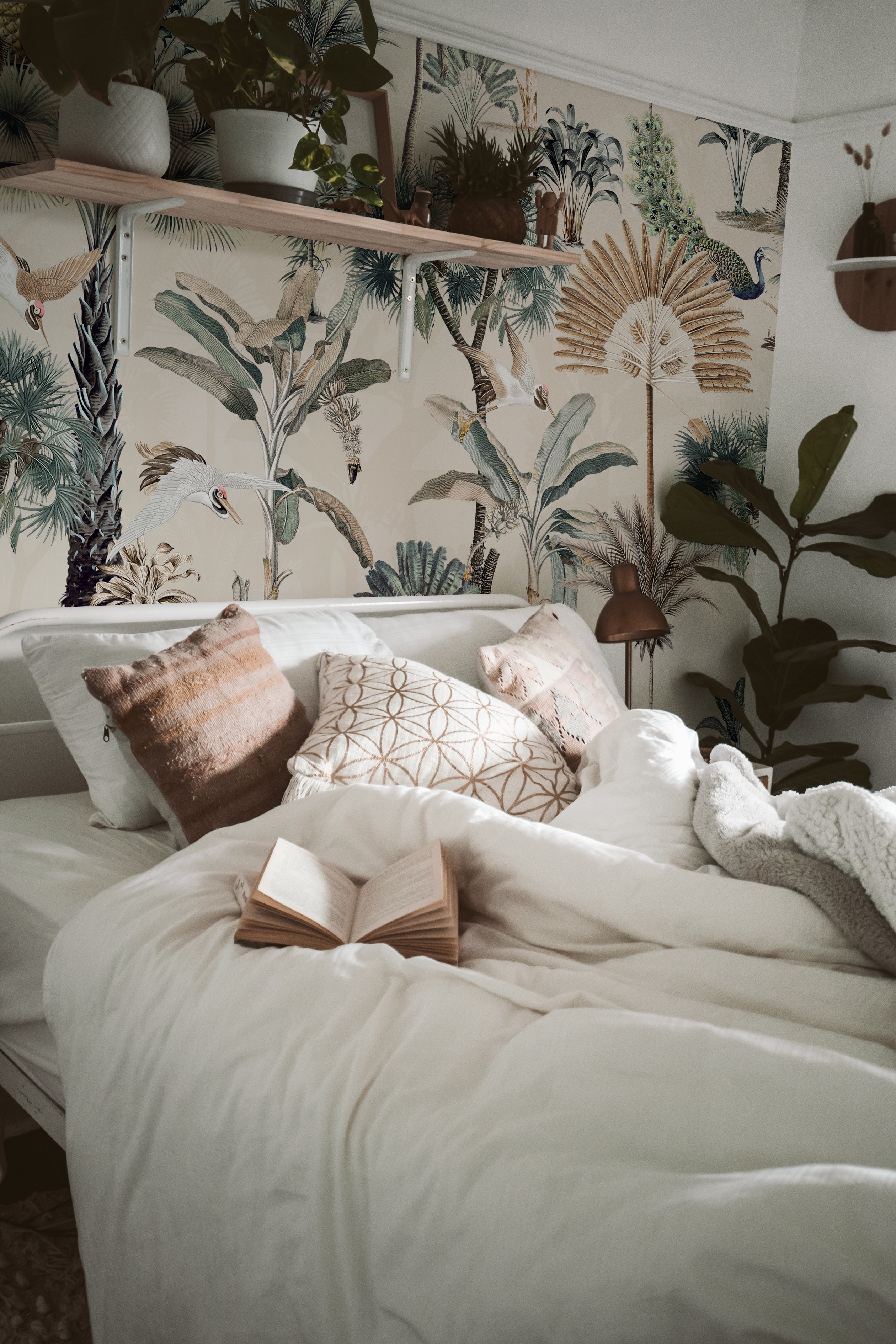 A cozy bedroom setting showcasing the Exotic Ecru Wallpaper on the wall behind the bed. The tropical motif, with its detailed depiction of various palms, birds, and exotic foliage, creates a lively yet soothing backdrop