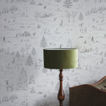 A close-up view of a room corner, where the winter-themed wallpaper provides an elegant backdrop to a vintage floor lamp with a green shade, highlighting the intricate details of the sketched wildlife and trees.