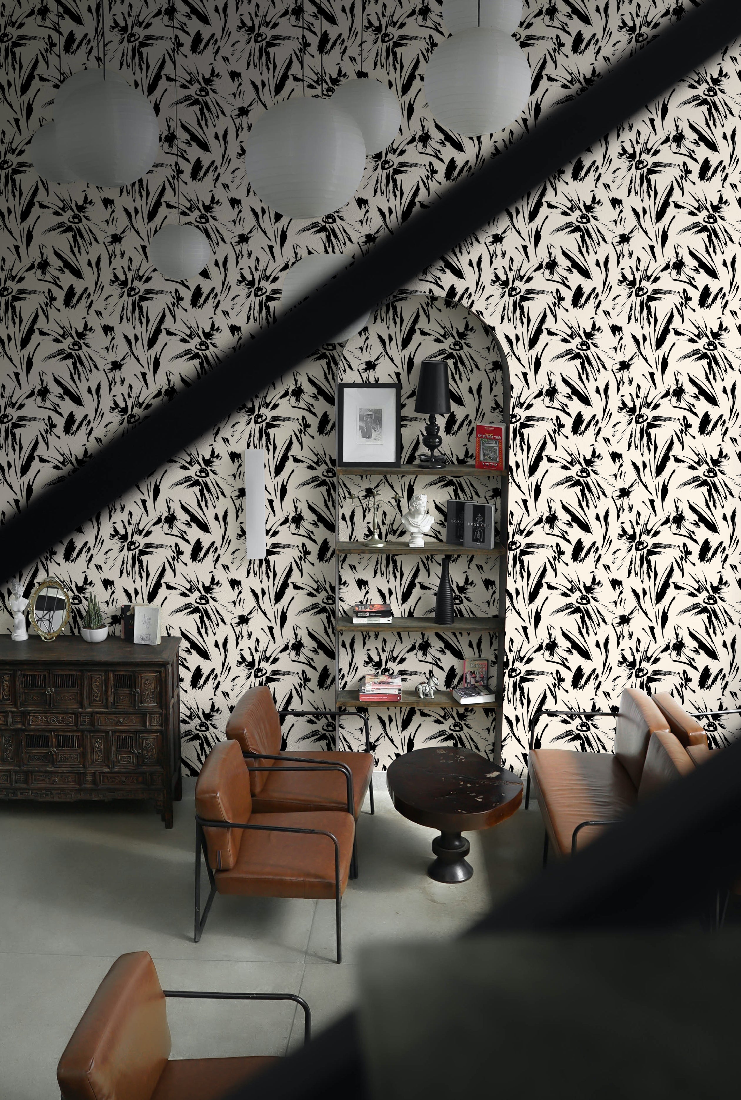 An elegant lounge area decorated with the Modern Floral Sketch Wallpaper - 25". The black on white abstract floral pattern provides a striking backdrop for the vintage brown leather furniture and eclectic decor, creating a sophisticated and contemporary space.