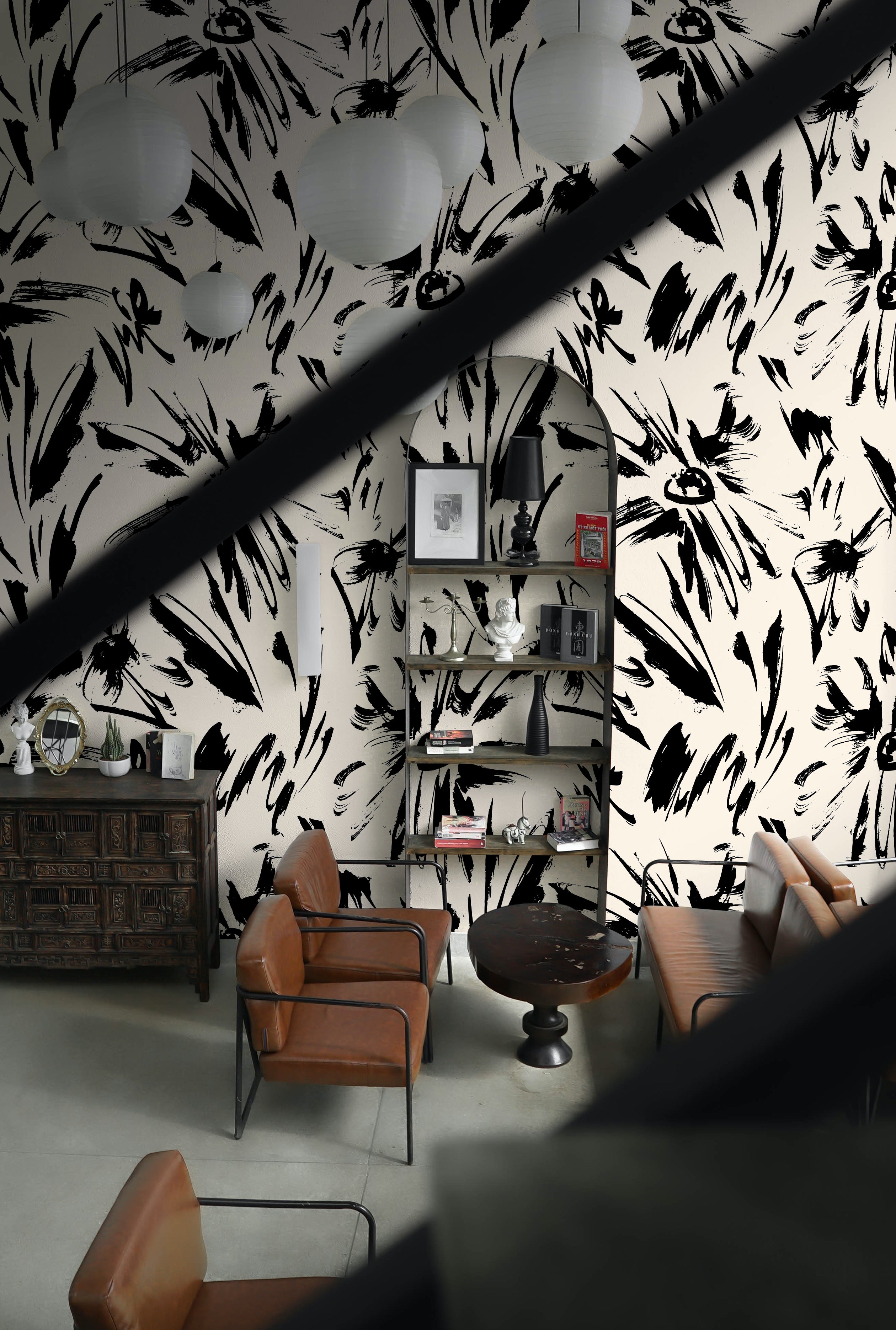 A stylish lounge area enhanced with the Modern Floral Sketch Wallpaper - 75", where the large black abstract floral patterns on a white background create a bold backdrop. The room features eclectic decor with vintage leather furniture and modern accessories, providing a chic and sophisticated environment.