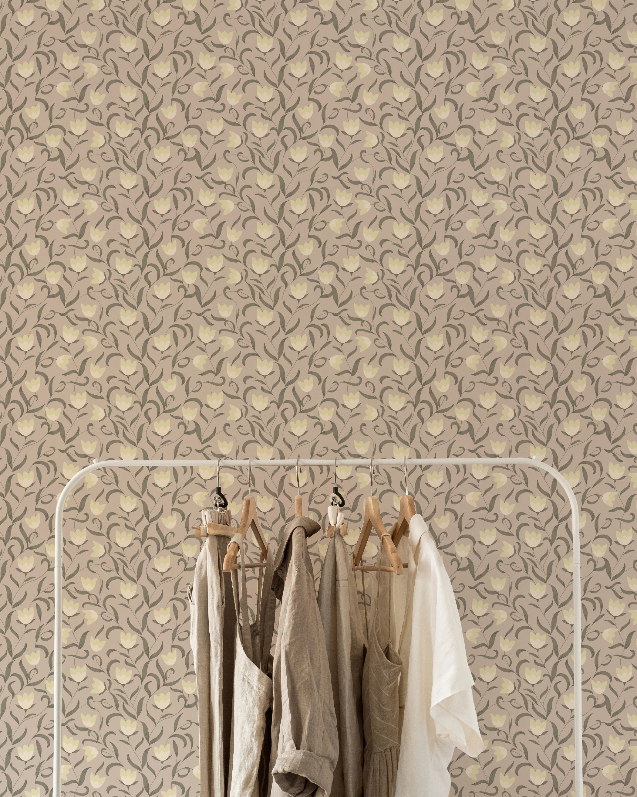 A clothing rack with neutral-toned garments hanging against a backdrop of Timeless Tulips Wallpaper, highlighting the wallpaper's graceful tulip and leaf design in soft, earthy colors.