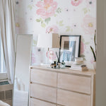 A stylish bedroom setup showcasing the Gentle Blossom Wallpaper - 75" on the main wall behind a contemporary wooden dresser and a large mirror. The wallpaper's lush pink floral pattern adds a touch of femininity and warmth, complementing the minimalistic decor and neutral furniture
