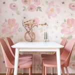 A charming dining area featuring the Gentle Blossom Wallpaper - 75" as a stunning backdrop. The wallpaper displays a pattern of pink and white flowers with soft green leaves, perfectly harmonizing with the pink chairs and white dining table, creating an inviting and elegant space