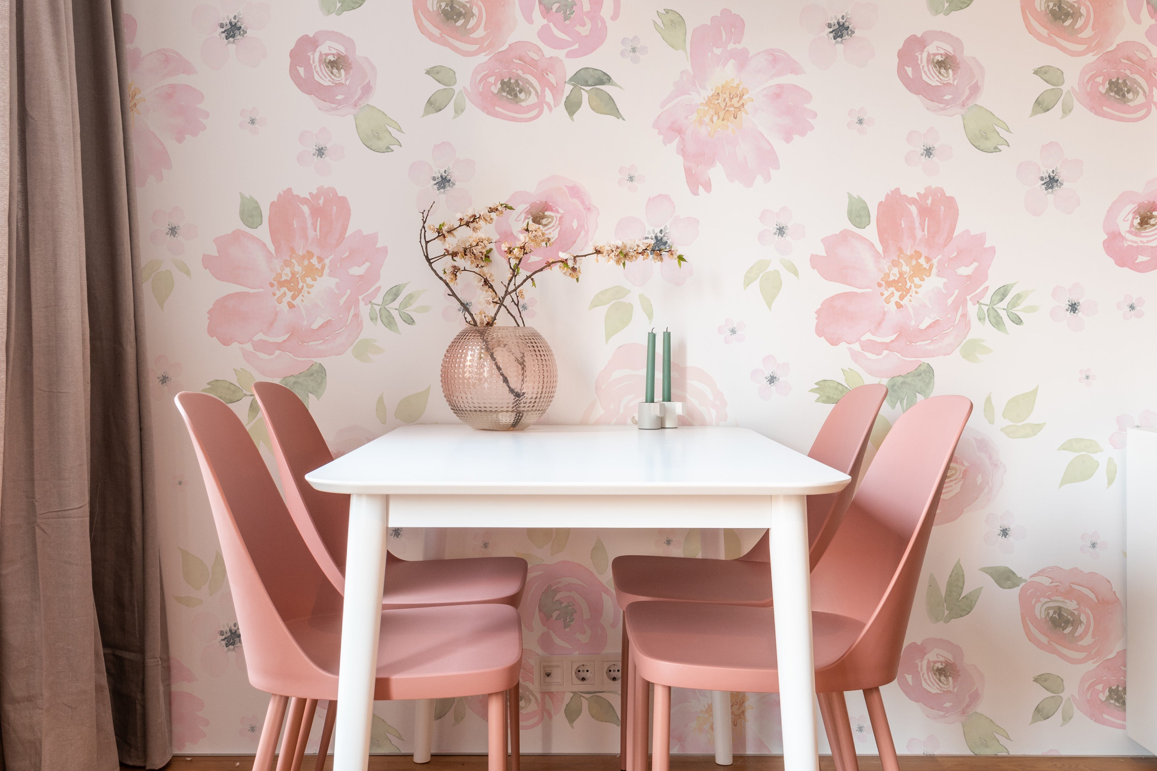 A charming dining area featuring the Gentle Blossom Wallpaper - 75" as a stunning backdrop. The wallpaper displays a pattern of pink and white flowers with soft green leaves, perfectly harmonizing with the pink chairs and white dining table, creating an inviting and elegant space