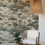 A cozy corner with a modern white armchair and a natural jute round rug on a wooden floor. An indoor potted plant sits beside the chair, and the room is illuminated by a large, tiered, fringe pendant light. The walls are covered with a safari-themed wallpaper mural depicting a savanna scene with impalas and a leopard amid a variety of trees