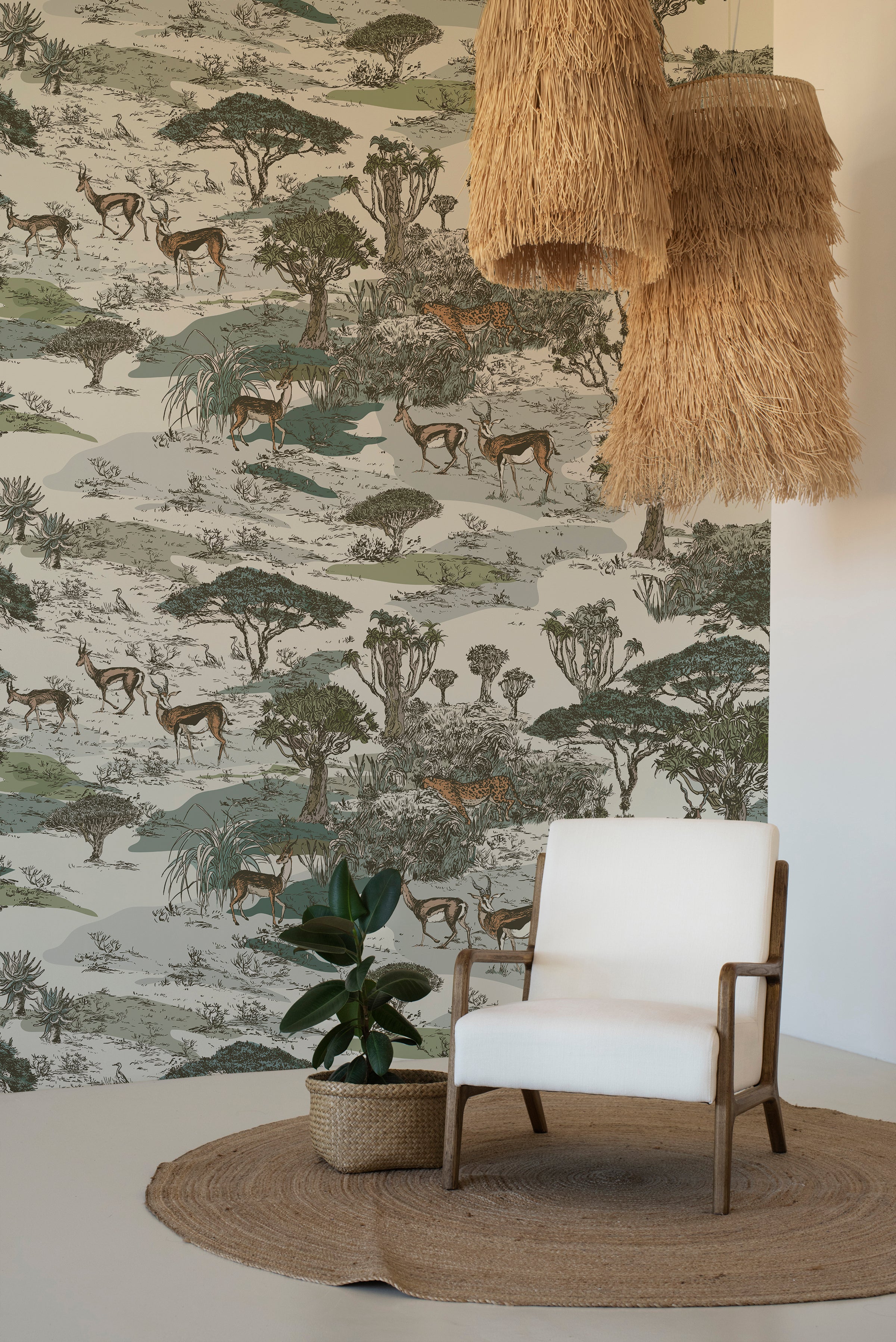 A cozy corner with a modern white armchair and a natural jute round rug on a wooden floor. An indoor potted plant sits beside the chair, and the room is illuminated by a large, tiered, fringe pendant light. The walls are covered with a safari-themed wallpaper mural depicting a savanna scene with impalas and a leopard amid a variety of trees