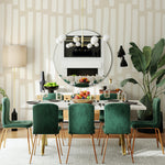 A stylish dining area enhanced with the Boardwalk Wallpaper - 100" adorning the walls, featuring tall, uneven beige stripes on a cream backdrop. The room is furnished with plush green velvet chairs and a round table under a chic circular mirror, creating a sophisticated and inviting space.