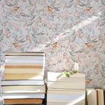 An inviting reading nook enhanced by the Light Flying Birds Wallpaper, which forms a beautiful backdrop with its floral and avian motifs. The wallpaper adds a bright and airy feel to the space, complemented by sunlight filtering through stacks of books.