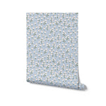 Rolls of Floral Love Wallpaper - Blue highlighting its beautiful design with small white flowers, green stems, and yellow centers on a soft blue background, ideal for adding a touch of elegance and tranquility to any room.