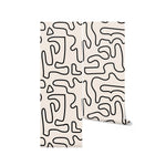 A roll of Abstract Doodle Wallpaper, unrolled slightly to reveal the design of black abstract lines on a beige background. The wallpaper features a dynamic and free-form doodle pattern that brings a creative and unique look to any space.