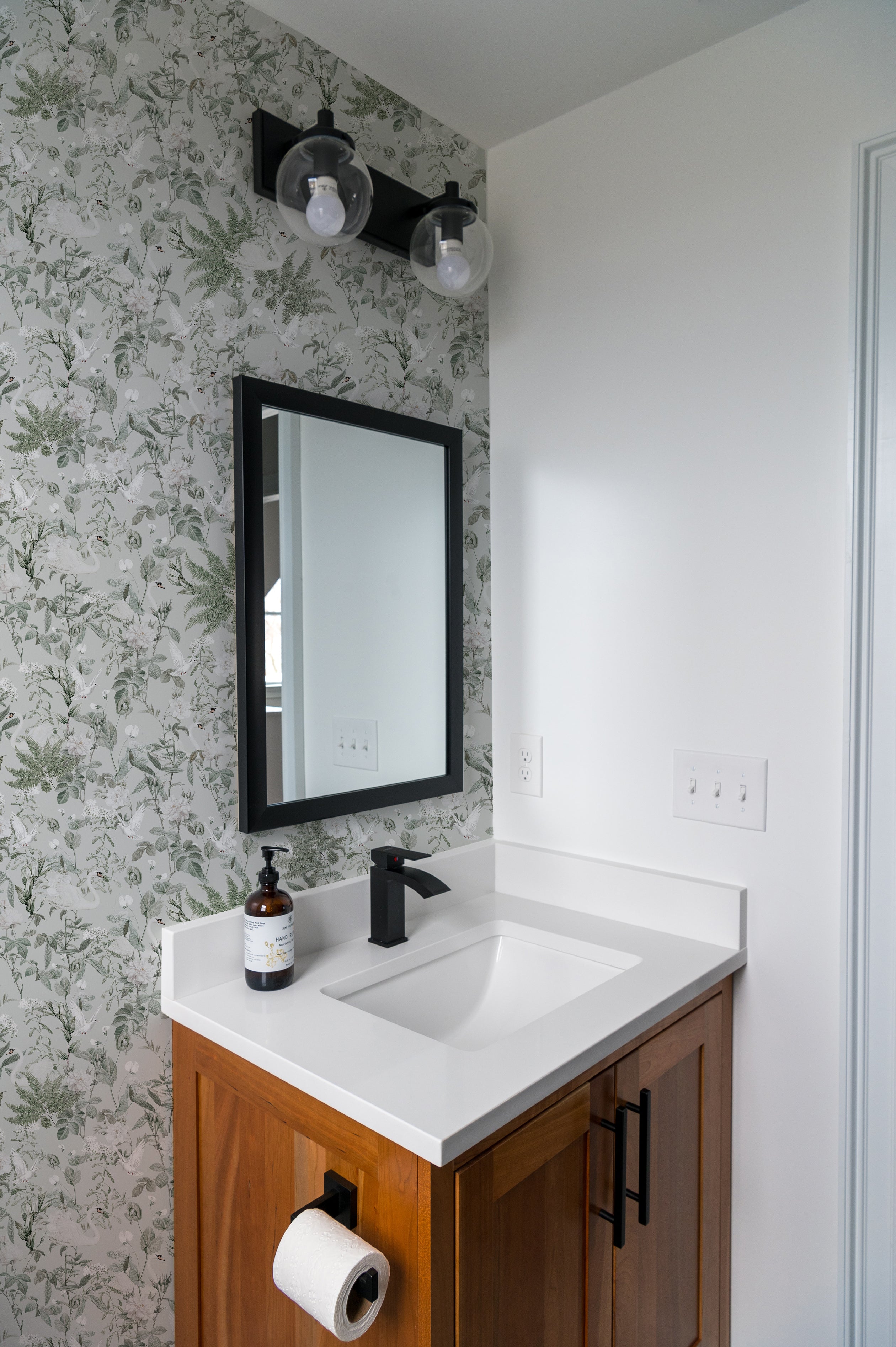 A modern bathroom enhanced by the Sage Bird Wallpaper, which wraps around the space, providing a calm and inviting ambiance. The wallpaper pairs well with the contemporary fixtures and wooden cabinetry, emphasizing the blend of nature and modern design.