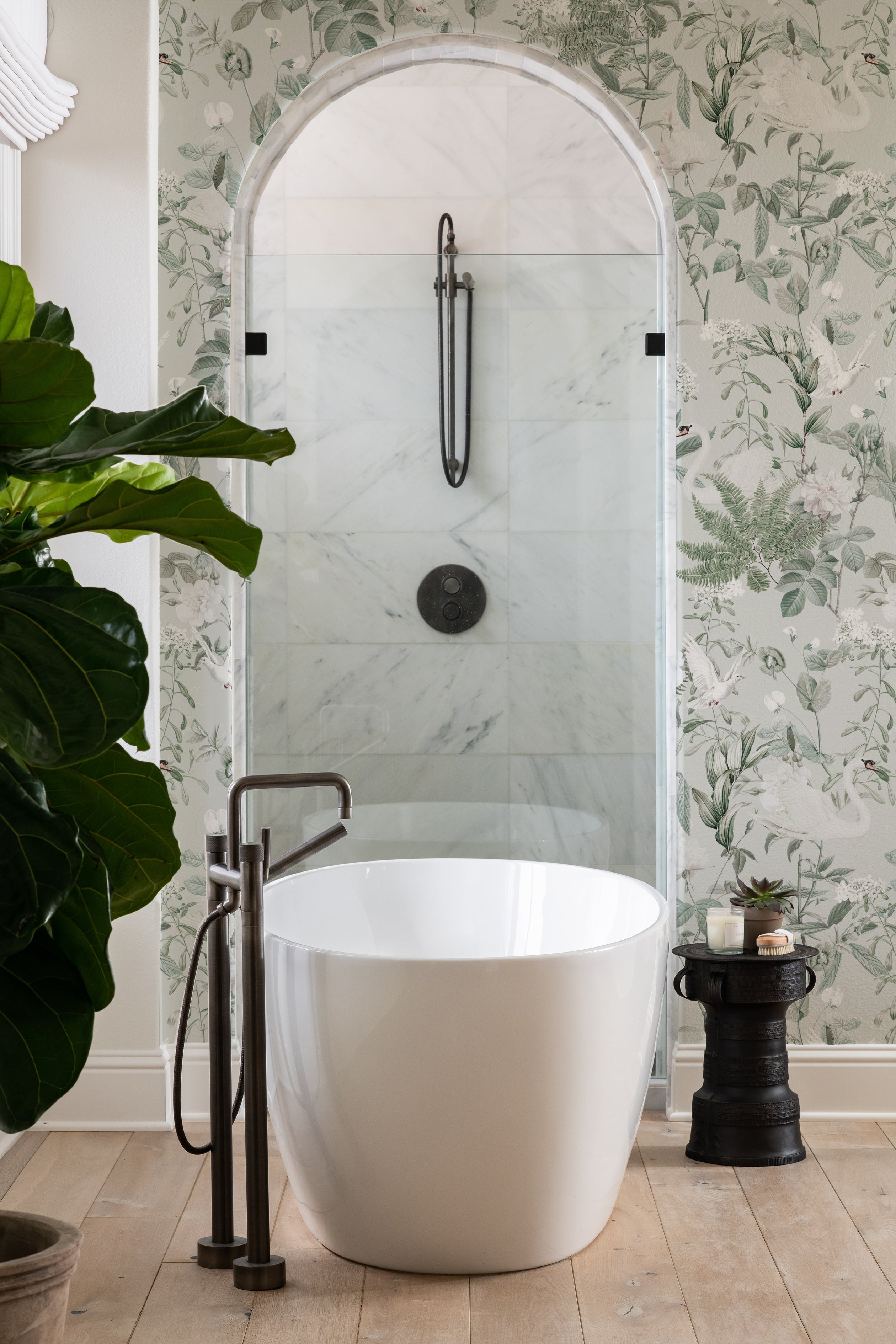 A luxurious bathroom showcasing Sage Bird Wallpaper as an accent wall behind a modern freestanding bathtub, with the wallpaper's white swans and green foliage complementing the clean lines and natural light of the space.