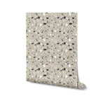 A roll of Earthen Terrazzo Wallpaper, partially unrolled to display the unique terrazzo pattern with a diverse mix of chip sizes and colors, ideal for adding a modern and artistic touch to any room's decor.