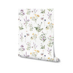 A roll of Midsummer Watercolour Bouquet Wallpaper with a white background adorned with an array of watercolor flowers and plants. The realistic portrayal of various wildflowers creates a vibrant and inviting pattern that captures the essence of a peaceful summer meadow