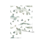 A roll of the "Wild Pinery Wallpaper" partially unrolled against a plain background, displaying the wallpaper's pattern of watercolor pine trees and birds. This image showcases the gentle color transitions and the free-form shapes that make up the design, offering a visual sense of the wallpaper's calming and artistic qualities.