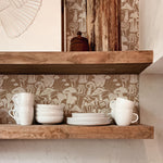 A rustic kitchen shelf scene set against a charming mushroom-patterned wallpaper in brown, showcasing an assortment of white cups and dishes, invoking an earthy and homey ambiance.