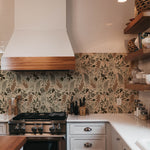 A modern kitchen with a stylish backsplash featuring owl and foliage pattern wallpaper in neutral tones, harmonizing with wooden shelves and white cabinetry