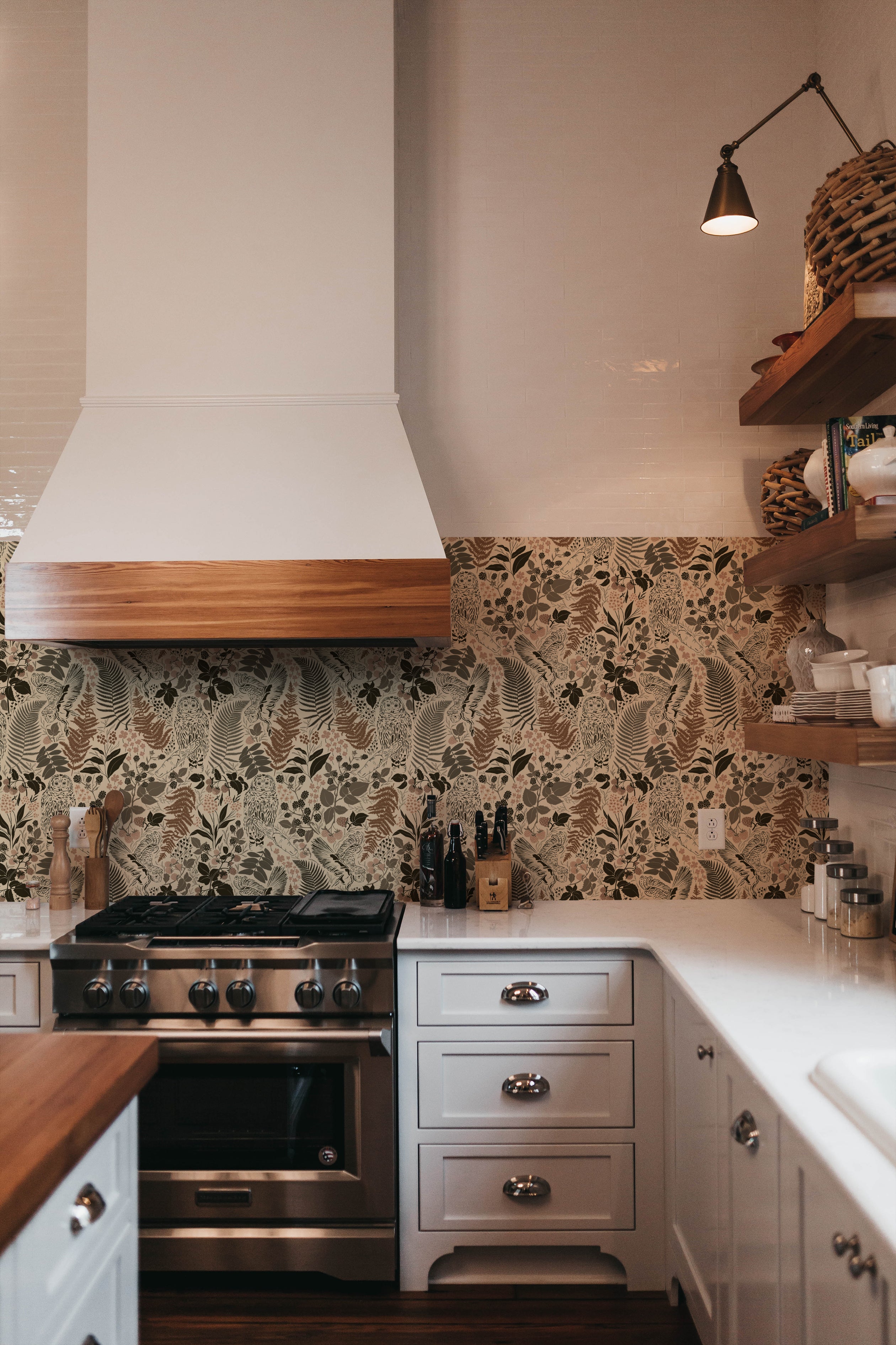 A modern kitchen with a stylish backsplash featuring owl and foliage pattern wallpaper in neutral tones, harmonizing with wooden shelves and white cabinetry