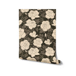 A roll of wallpaper with a repeating pattern of stylized cream roses and olive green leaves on a dark background, suggesting an elegant and contemporary design suitable for various interior decor styles.