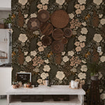 A stylish kitchen space enhanced with Forest Wildflower Wallpaper, which displays an elaborate pattern of white and peach wildflowers against a dark, leafy background. The wall is adorned with various woven baskets, adding a rustic charm to the floral scene.