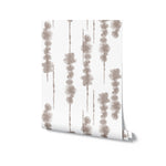 A roll of 'Shibori Watercolour Wallpaper' is displayed, slightly unrolled to show the unique pattern of beige watercolor shibori stripes, ready to impart an effortless and modern touch to any interior design scheme.