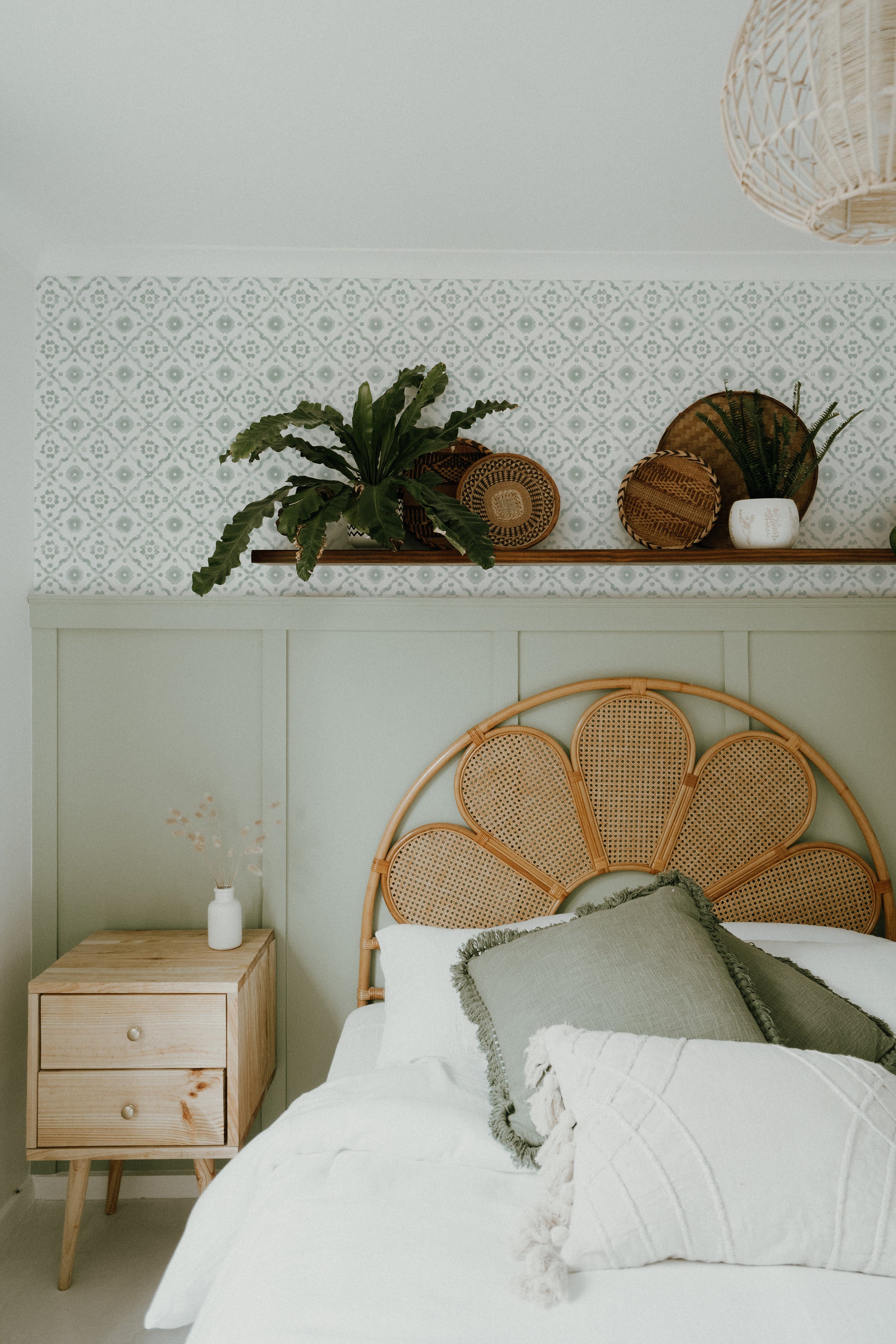 A stylish bedroom setting enhanced by the Euclid Wallpaper, featuring pale blue geometric flower patterns on a white backdrop. The room is complemented by a natural wicker headboard and matching decor items, creating a serene and inviting atmosphere.