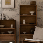 A rustic wooden bookcase against a backdrop of Outdoor Friend Sketch Wallpaper, featuring detailed sketches of outdoor scenes with hunters, dogs, and wildlife in a monochrome style. The decor includes various ceramic and wooden items, enhancing the naturalistic theme