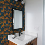 A stylish bathroom adorned with Autumn Boho wallpaper that surrounds a black-framed mirror and a modern vanity with a black faucet, highlighting the bold, floral pattern in a vibrant mix of blue and orange.
