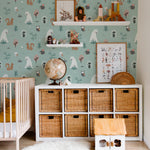 This nursery room is beautifully decorated with "Kids Wallpaper - Forest Critters - 25 inches." The wallpaper features a delightful scene of forest animals including bears, squirrels, and owls among trees and plants, set against a soft teal background. The room is furnished with a white crib, rattan storage units, and playful decor, creating a charming and inviting space for children.