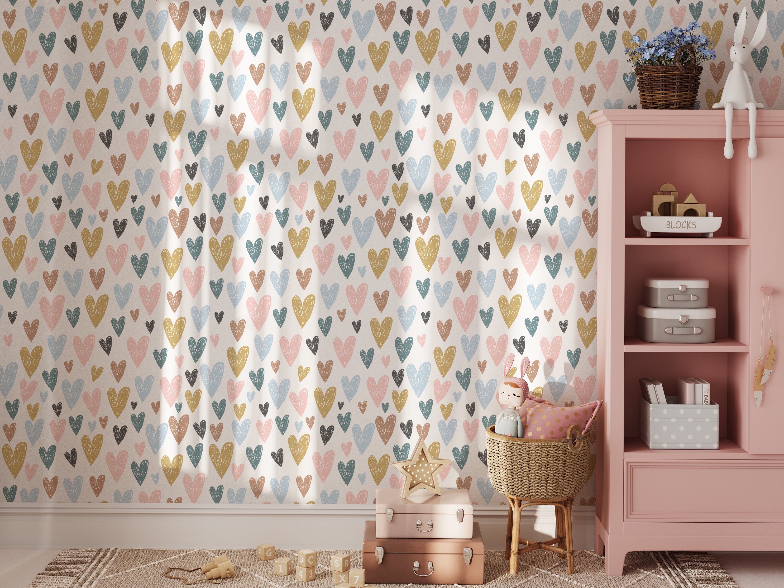 A child`s play area with a pink dresser and with a beautiful background of the Amore wallpaper. The wallpaper features a pattern of multicolored hearts in shades of blue, pink, yellow, and black, creating a playful and loving atmosphere suitable for a child's bedroom.