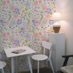 A simple yet stylish workspace with Romana Wallpaper, adorned with an array of colorful flowers in pink, blue, and yellow. A white table and chairs set against the floral backdrop creates a bright and airy study area