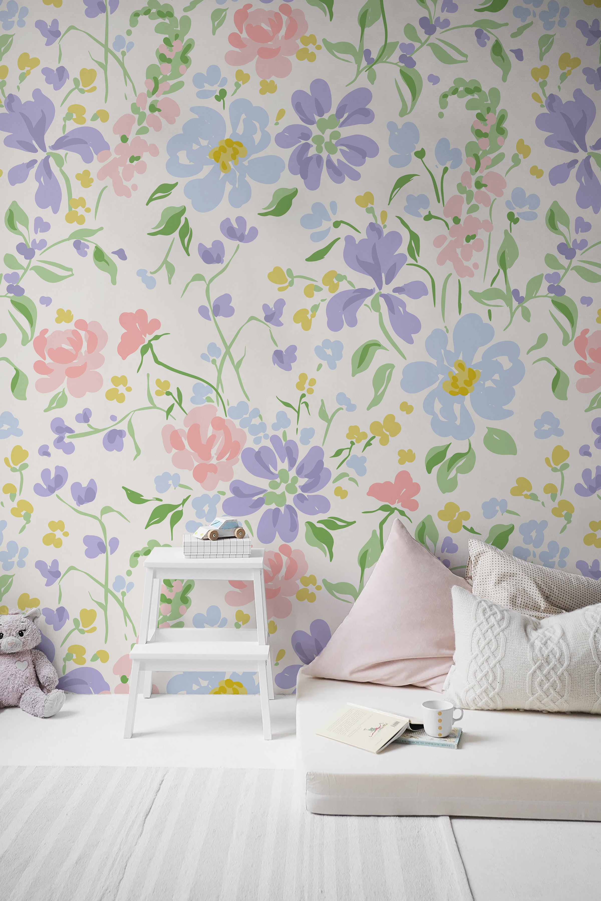 A cozy corner of a child's room decorated with Romana Wallpaper showcasing a vibrant floral pattern in soft pastels. A white bed and step stool are complemented by a pale pink pillow and a cuddly toy, creating a peaceful and playful ambiance