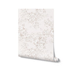 A single roll of 'Rose Bouquet Wallpaper' leaning against a white background. The wallpaper displays an elegant floral pattern with bouquets of roses in shades of grey on a soft, off-white linen texture.