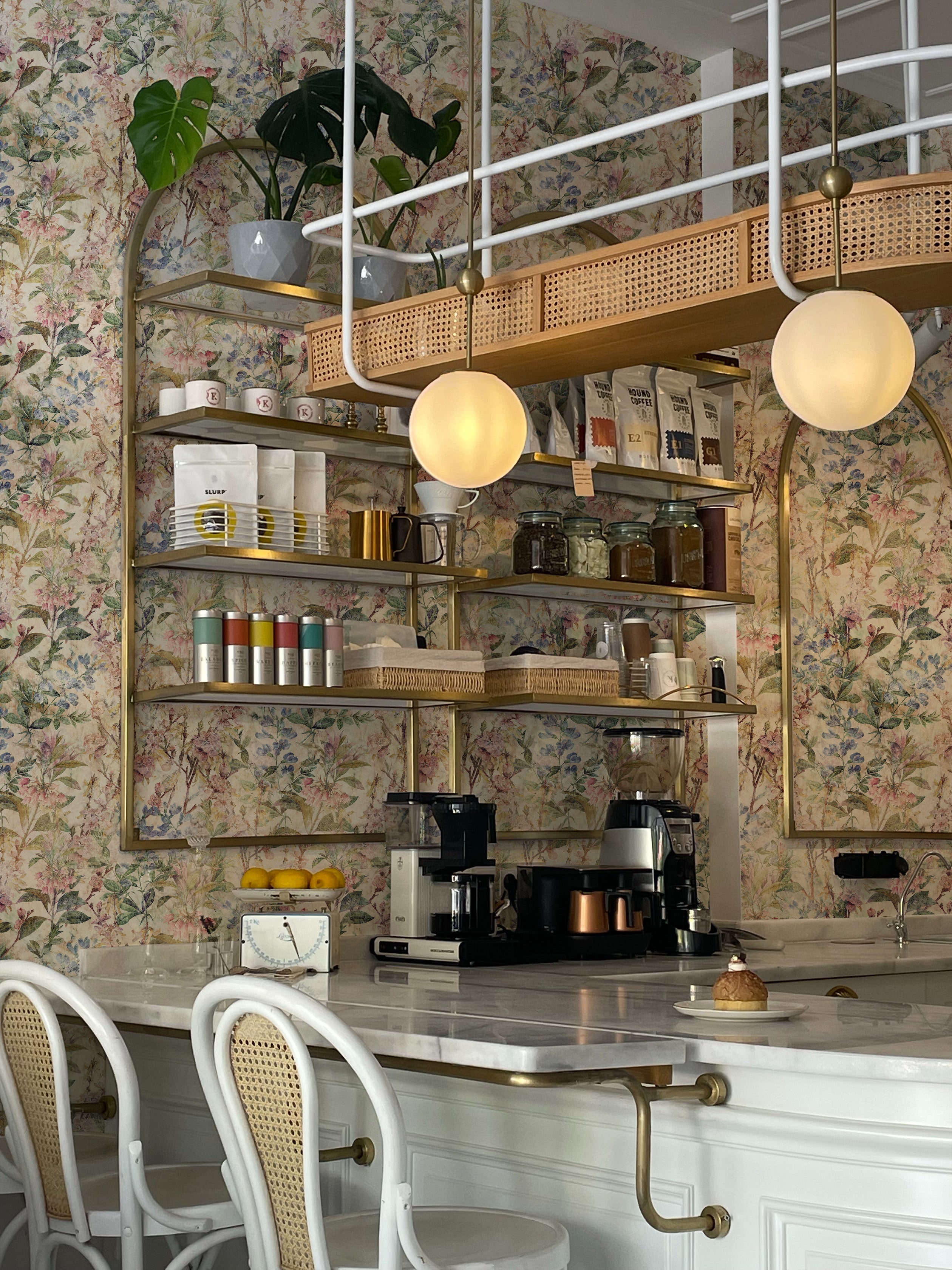 A sophisticated kitchen space with a ceiling-mounted storage shelf adorned with the "Ancient Florals Wallpaper." The wallpaper features a detailed print of varied flowers and plants in pastel colors, enhancing the romantic vintage aesthetic of the room.