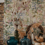 A close-up view of the "Ancient Florals Wallpaper" showcasing its intricate botanical print. The wallpaper decorates a room corner styled with dried flowers in vases and seasonal pumpkins, contributing to a rustic and quaint interior design.