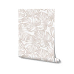 A square image presenting a rolled-up piece of wallpaper with a monstera leaf design, emphasizing its texture and watercolor-like aesthetic. The soft gray and white hues of the leaves provide a modern and elegant feel, with the roll resting against a plain backdrop to highlight the pattern.