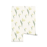 A roll of Bright Garden Flowers Wallpaper, slightly unrolled to show the pattern of delicate yellow tulips and green foliage against a cream backdrop. This wallpaper offers a subtle yet vibrant touch, perfect for enhancing spaces with natural beauty and a splash of color.