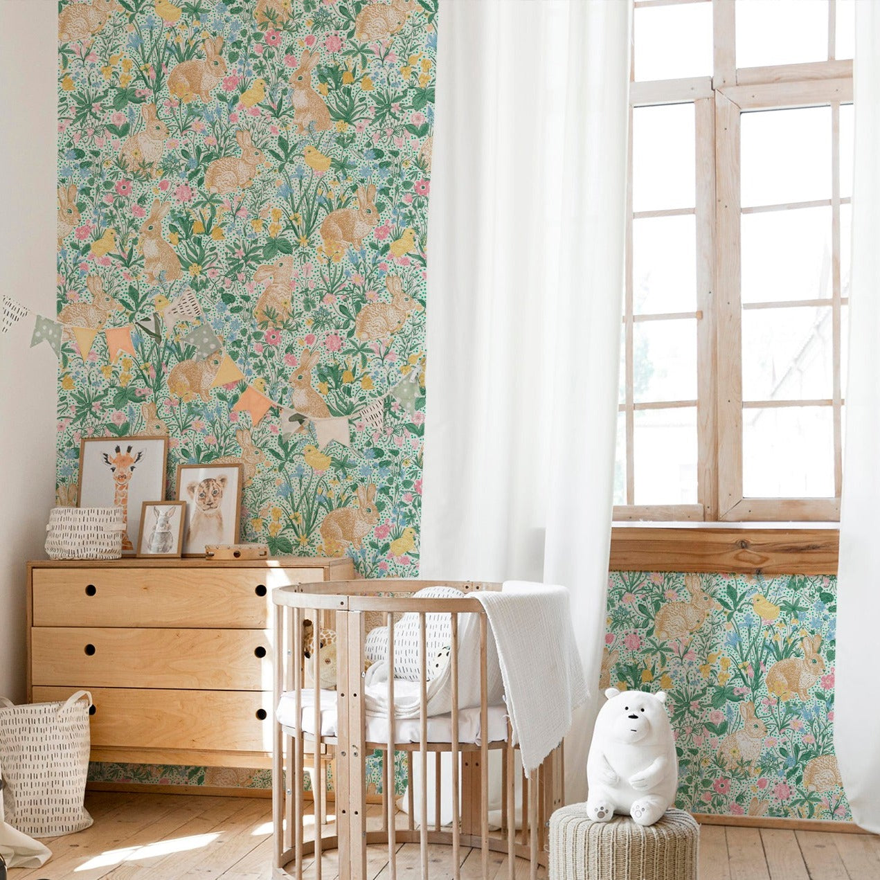 Bright and airy children's room featuring a colorful floral wallpaper with rabbits, birds, and a variety of flowers. The room includes wooden furniture, a circular crib, and playful decor items like a small ride-on car and a hopscotch rug."