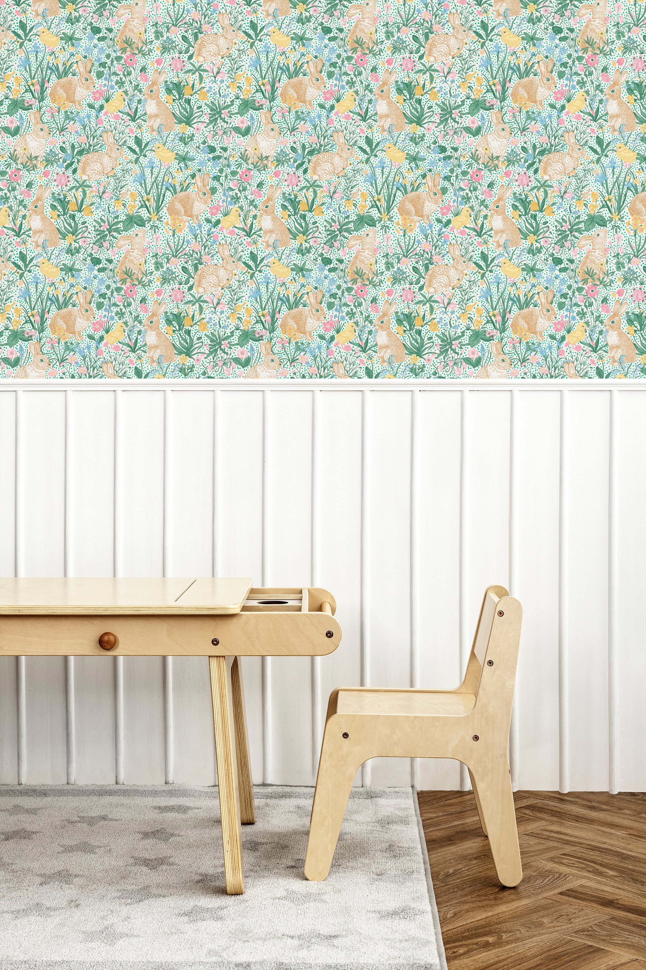Close-up of a vibrant children's wallpaper depicting a lush, floral scene with rabbits and various spring flowers in soft pastel colors. Positioned beside a simple wooden desk and chair set, enhancing a calm study environment.