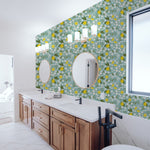 A stylish bathroom featuring Lemon + Jasmine Wallpaper with a light blue background adorned with vibrant lemon and white jasmine flowers. The space includes a white freestanding bathtub, a wooden double-sink vanity, and circular mirrors, creating a fresh and bright atmosphere.