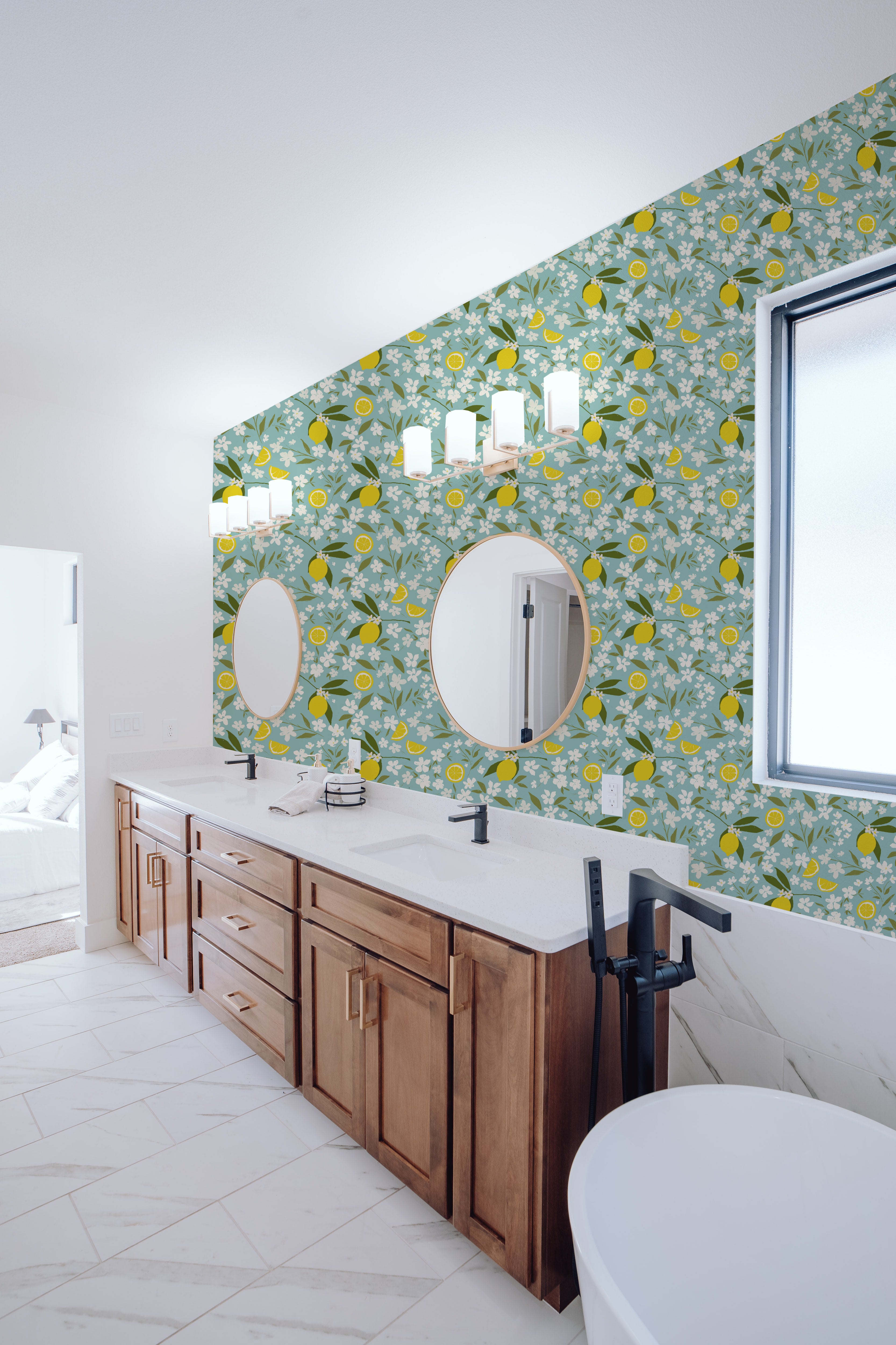A stylish bathroom featuring Lemon + Jasmine Wallpaper with a light blue background adorned with vibrant lemon and white jasmine flowers. The space includes a white freestanding bathtub, a wooden double-sink vanity, and circular mirrors, creating a fresh and bright atmosphere.