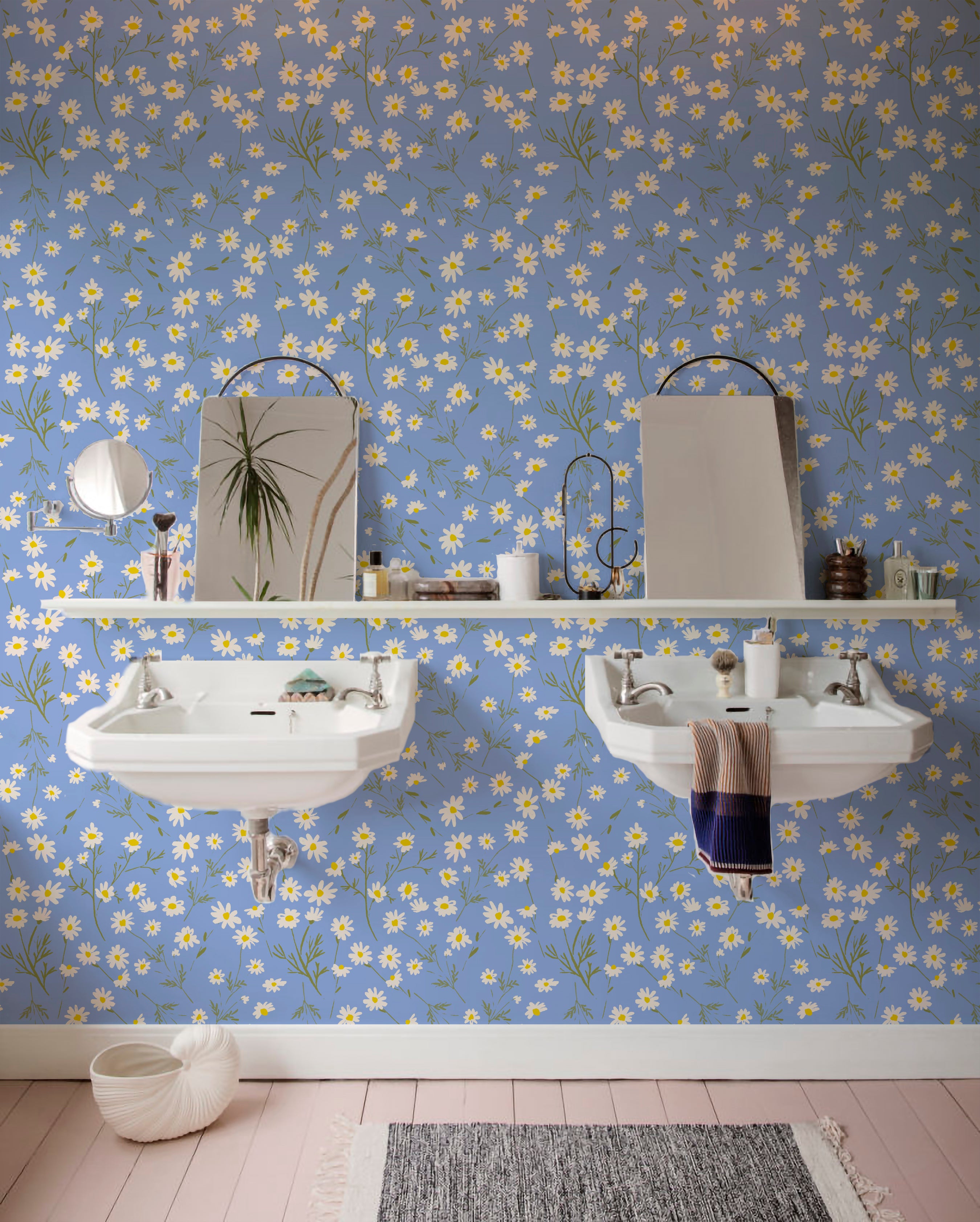 Spacious bathroom with twin white pedestal sinks against a wall covered in a blue floral wallpaper with white and yellow daisy patterns, complemented by a pink wooden floor and various bathroom accessories.